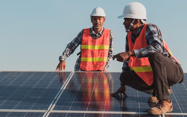 two workers in hard hats and reflective vests working on solar panels