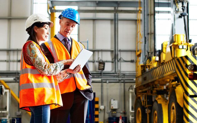 manufacturing workers in protective gear working on tablet in a warehouse