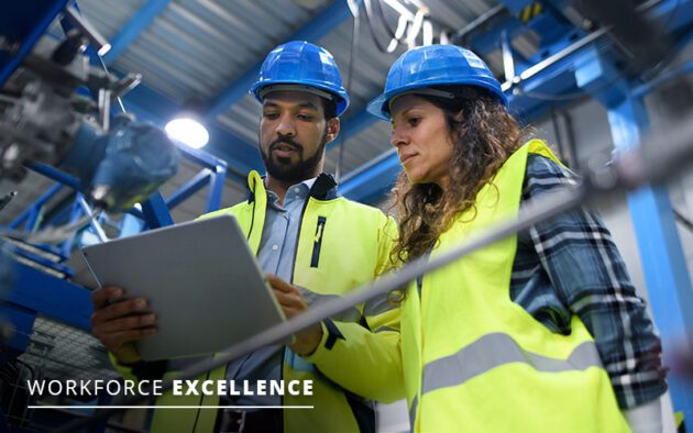 Two workers wearing safety gear review information on a tablet in an industrial setting. The words “Workforce Excellence” are displayed in the bottom left corner.